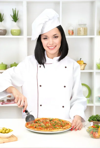 Hermosa chica jefe de cocina con pizza en el fondo de la cocina — Foto de Stock