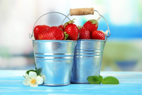 Ripe sweet strawberries in metal pails on blue wooden table — Stock Photo, Image