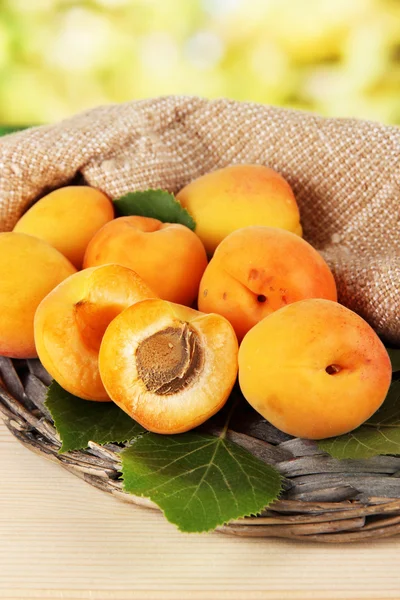 Apricots on wicker coasters on wooden table on nature background — Stock Photo, Image