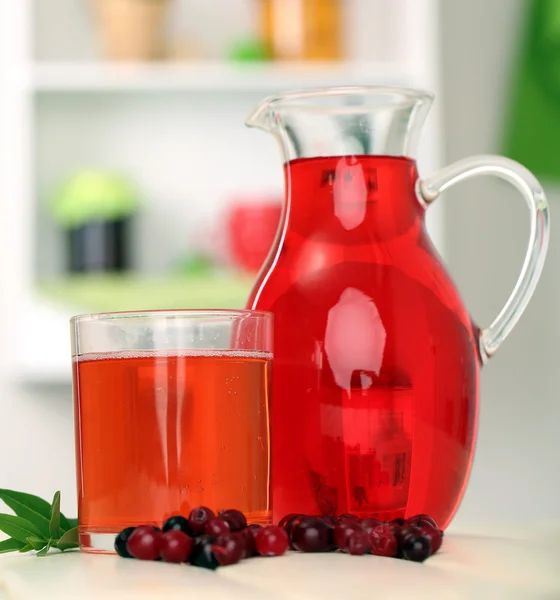 Кувшин и стакан клюквенного сока с красной клюквой на столе — стоковое фото