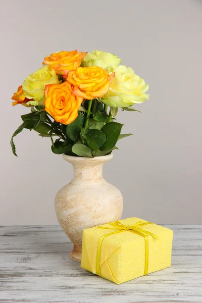 Beau bouquet de roses en vase avec cadeau sur table sur fond gris — Photo