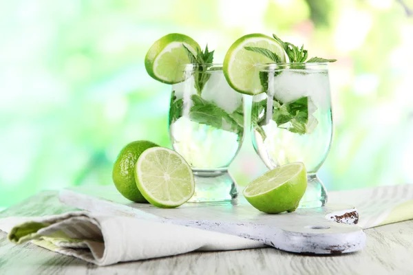 Glasses of cocktail with ice on board on napkin on wooden table on nature background — Stock Photo, Image