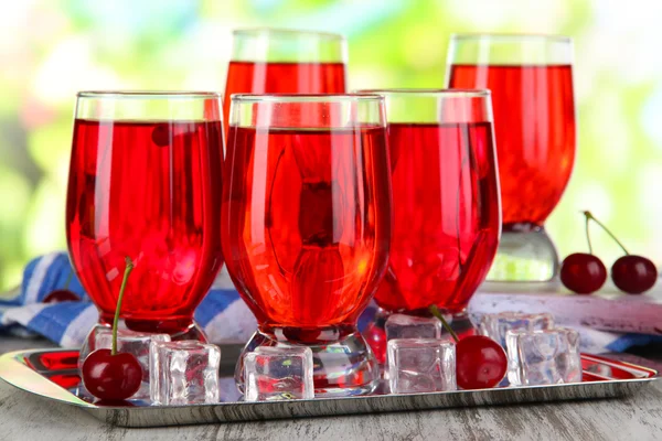 Glasses compote on board and metal tray on napkin on wooden table on nature background — Stock Photo, Image