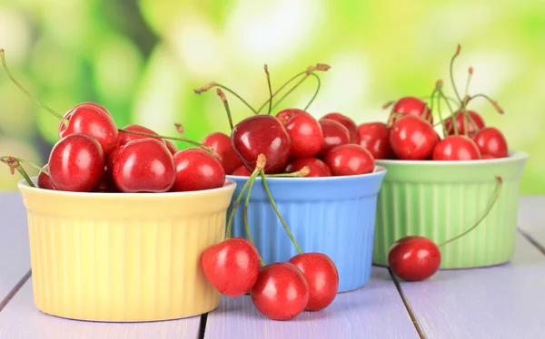 Bayas de cereza en cuencos sobre mesa de madera sobre fondo brillante — Foto de Stock