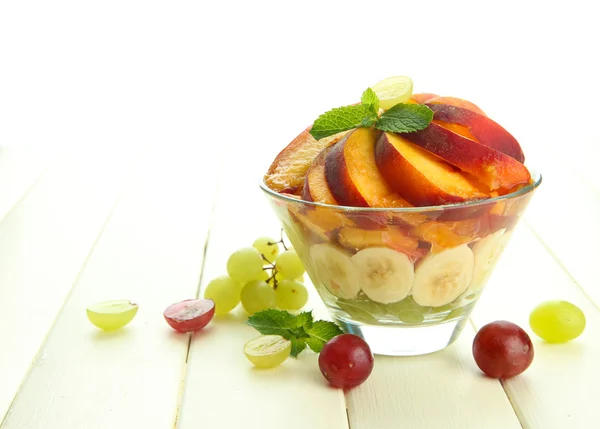 Ensalada de frutas sabrosas en cuenco de vidrio, sobre mesa de madera blanca —  Fotos de Stock