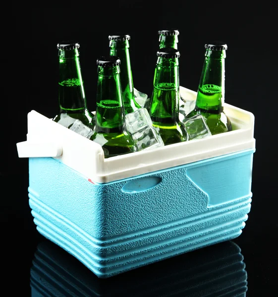 Bottles of beer with ice cubes in mini refrigerator, on black background — Stock Photo, Image