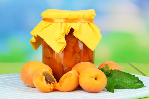 Apricot jam in glass jar and fresh apricots, on wooden table, on bright background — Stock Photo, Image