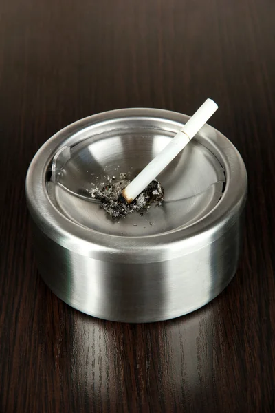 Kovový popelník a cigaret na dřevěný stůl — Stock fotografie