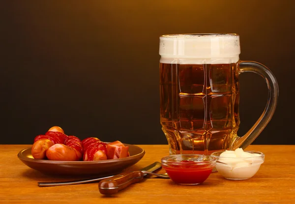 Cerveja e salsichas grelhadas em mesa de madeira sobre fundo marrom — Fotografia de Stock