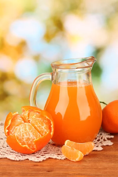 Jarro cheio de suco de tangerina, na mesa de madeira no fundo brilhante — Fotografia de Stock