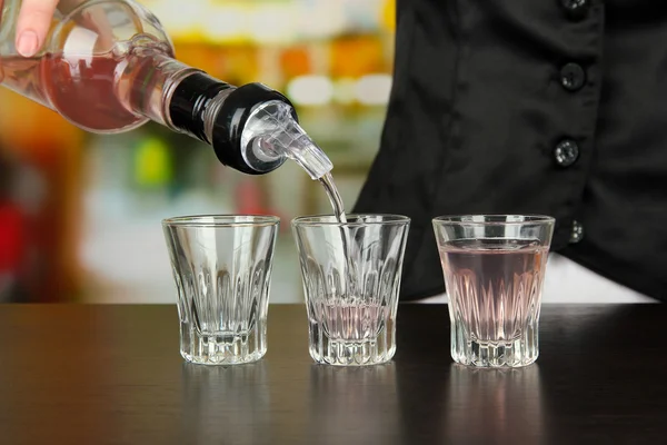 Barmen hand with bottle pouring beverage into glasses, on bright background — Stock Photo, Image