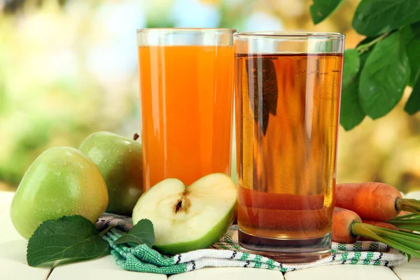 Glas juice, äpplen och morötter på vita träbord, på grön bakgrund — Stockfoto