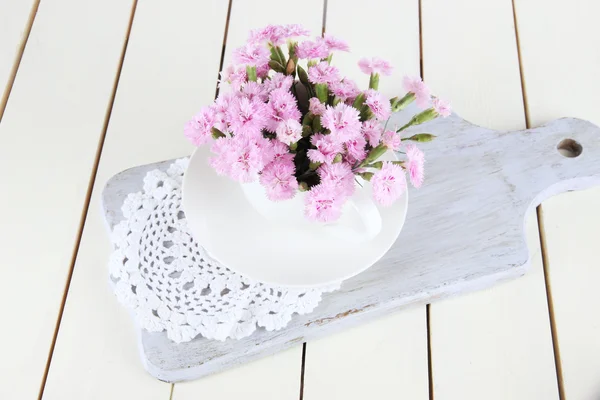 Nombreux petits clous de girofle roses en tasse sur planche en bois sur fond beige — Photo