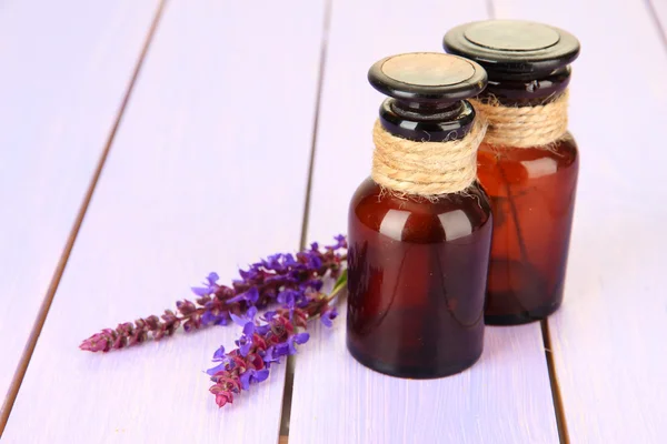 Botellas de medicina y flores de salvia sobre fondo de madera púrpura — Foto de Stock