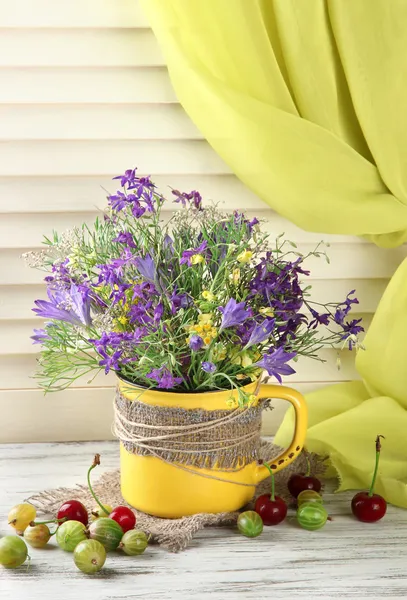 Hermoso ramo de flores silvestres en taza y bayas en mesa de madera —  Fotos de Stock