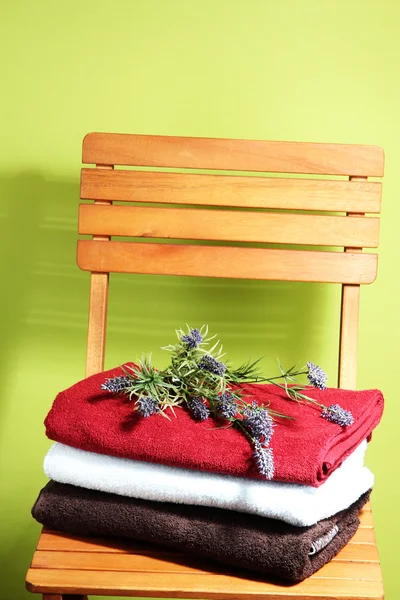 Towels and flowers on wooden chair on green background — Stock Photo, Image