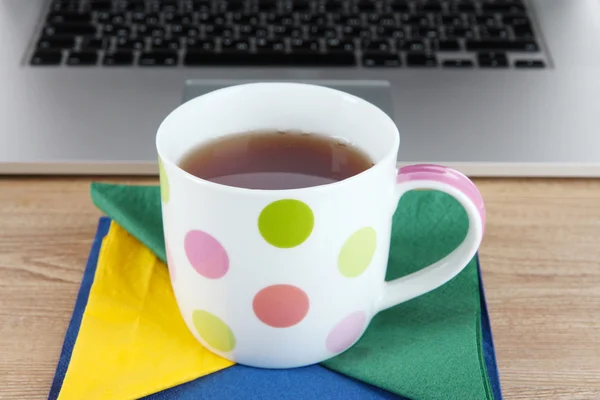 Tasse auf Serviette auf Laptop-Hintergrund auf Holztisch — Stockfoto