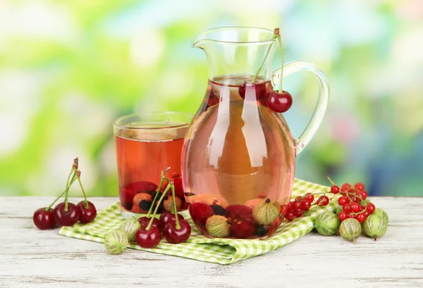Pitcher and glass of compote with summer berries on natural background — Stock Photo, Image