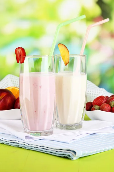 Leckere Milchshakes mit Erdbeeren und Pfirsich auf Holztisch vor natürlichem Hintergrund — Stockfoto