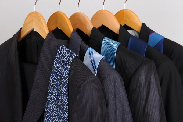 Garnitury i krawaty na wieszaki na szarym tle — Zdjęcie stockowe