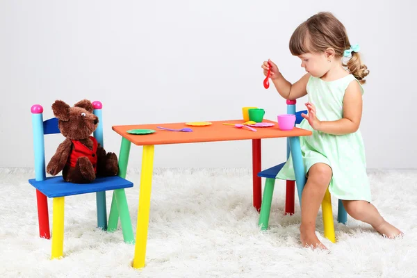 Pequena menina bonita sentada na pequena cadeira perto da mesa, no fundo cinza — Fotografia de Stock