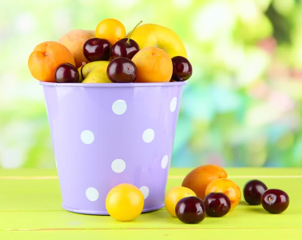 Яркие летние фрукты в ведре на деревянном столе на естественном фоне — стоковое фото