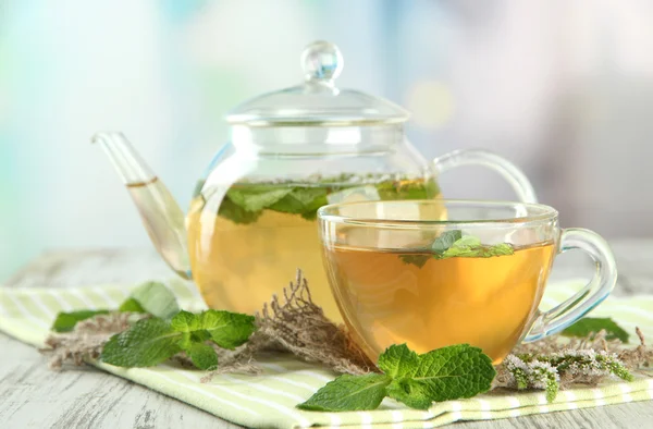 Teekanne und Tasse Kräutertee mit frischen Minzblüten auf Holztisch — Stockfoto