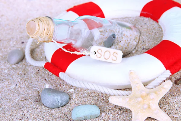 Glass of bottle with note inside on sand background — Stock Photo, Image