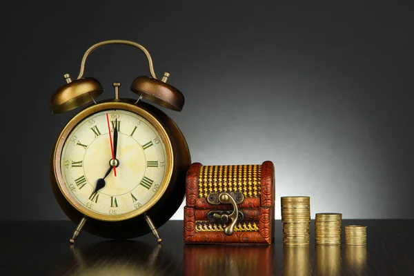 Orologio antico e monete su tavolo in legno su sfondo nero Foto Stock