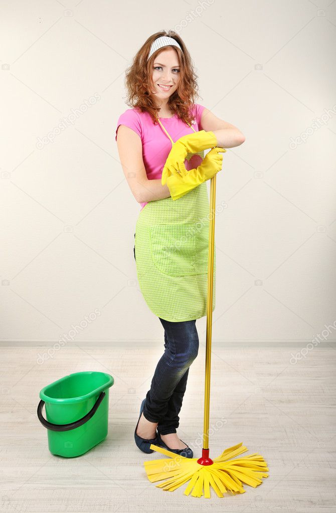 Young housewife with mop in room on grey background