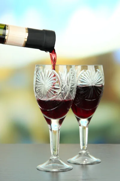 Rött vin som hälls i glas vin, på ljus bakgrund — Stockfoto