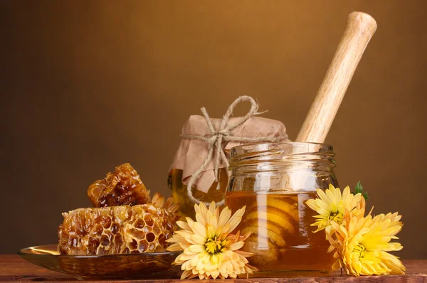 Twee potten van honing, honingraten en houten drizzler op tafel op gele achtergrond — Stockfoto