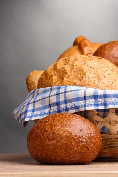 Delicioso pão na cesta na mesa de madeira no fundo cinza — Fotografia de Stock