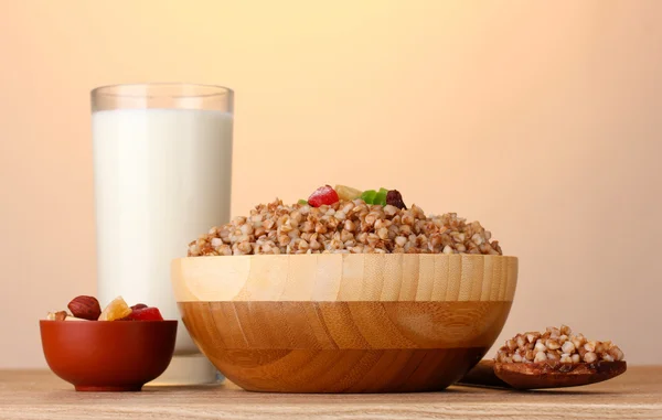 Boiled buckwheat in a wooden bowl with a glass of milk on wooden table on brown — Stock Photo, Image