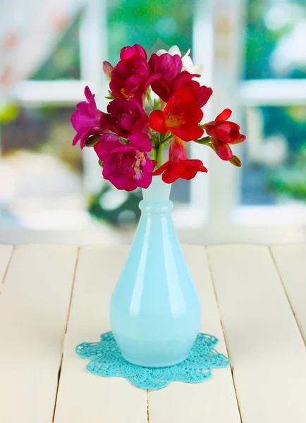 Belo buquê de freesia em vaso azul na mesa de madeira no fundo da janela — Fotografia de Stock