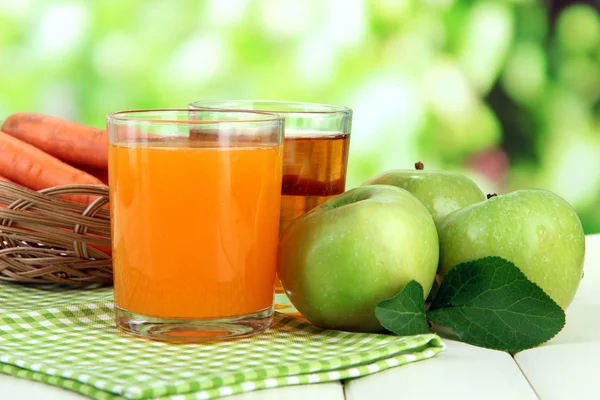 Glasses of juice, apples and carrots on white wooden table, on green background — Stock Photo, Image