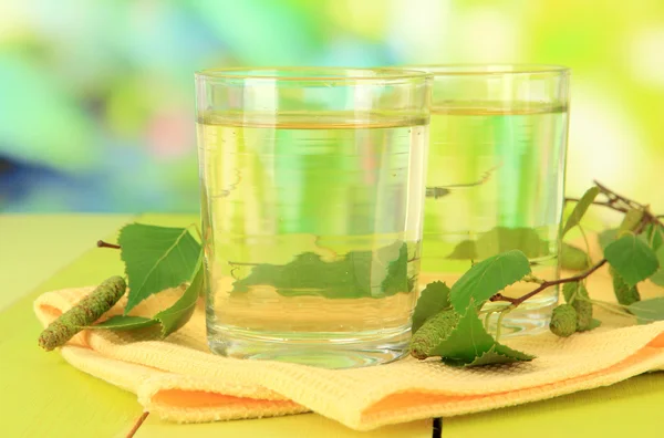 Glasses of birch sap on wooden table, on green background — Stock Photo, Image