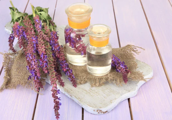 Geneeskundeflessen met salvia bloemen op paarse houten achtergrond — Stockfoto