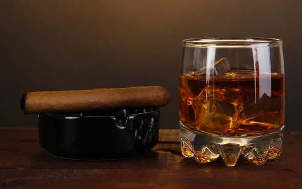 Brandy glass with ice and cigar on wooden table on brown background — Stok fotoğraf