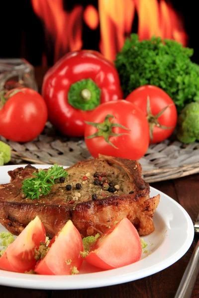 Trozo de carne frita en el plato en la mesa de madera sobre fondo de fuego — Foto de Stock