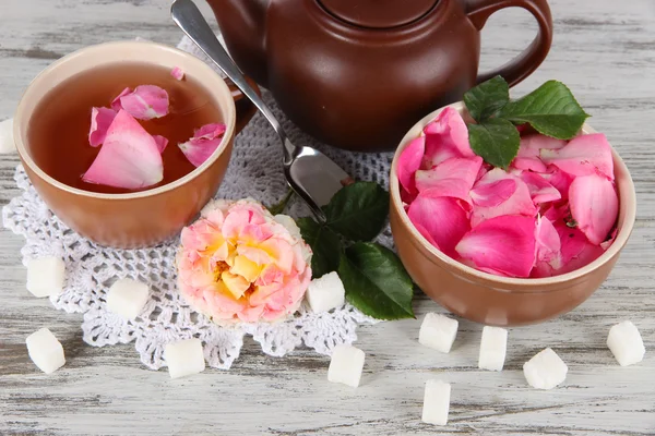 Konvice a šálek čaje z tea rose na palubě na ubrousek na dřevěný stůl — Stock fotografie