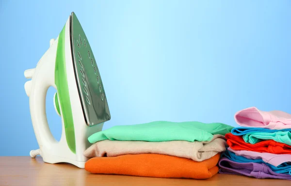 Steam iron with clothes, on color background — Stock Photo, Image