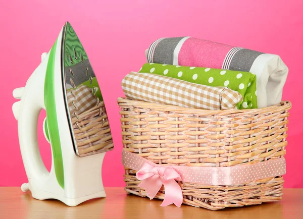 Steam iron and wicker basket with clothes, on color background — Stock Photo, Image