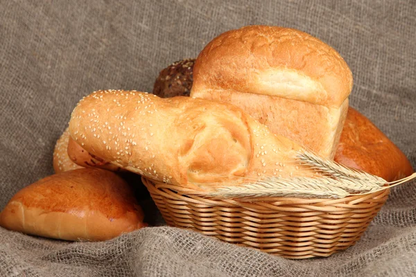 Nybakat bröd i rotting korg på säckväv bakgrund — Stockfoto