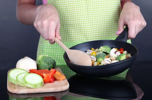 Mains faisant cuire le ragout de légumes dans une casserole sur fond gris — Photo