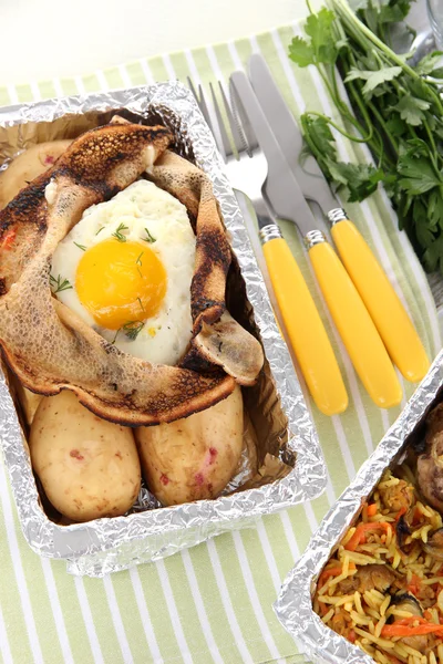 Food in boxes of foil on tablecloth — Stock Photo, Image