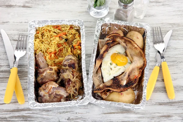 Food in boxes of foil on wooden table — Stock Photo, Image