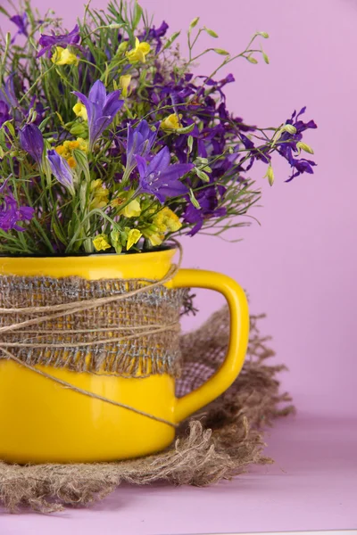 Mooi boeket van wilde bloemen in cup op paarse achtergrond — Stockfoto