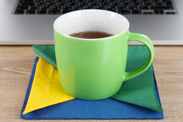 Grüne Tasse auf Serviette auf Laptop-Hintergrund auf Holztisch — Stockfoto