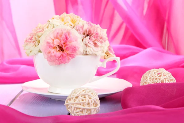 Rose in tazza sul tavolo di legno su sfondo panno rosa — Foto Stock